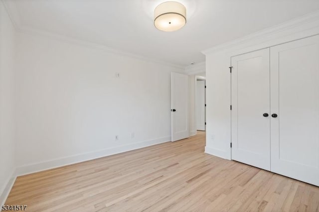 unfurnished bedroom featuring a closet, baseboards, light wood-style flooring, and crown molding