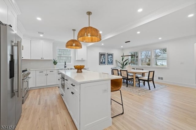 kitchen with a kitchen island, stainless steel appliances, light wood-style floors, a breakfast bar area, and light countertops