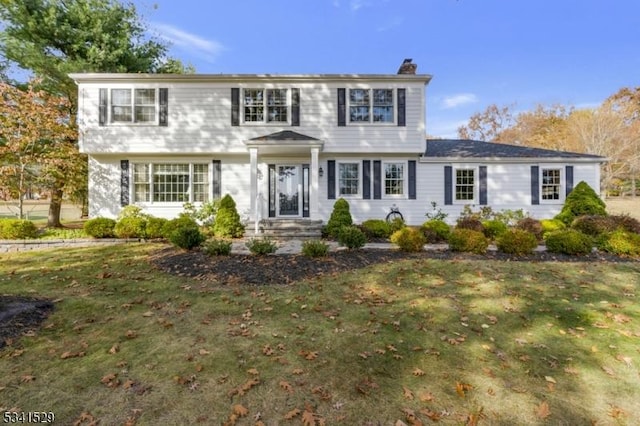 colonial inspired home featuring a chimney and a front yard