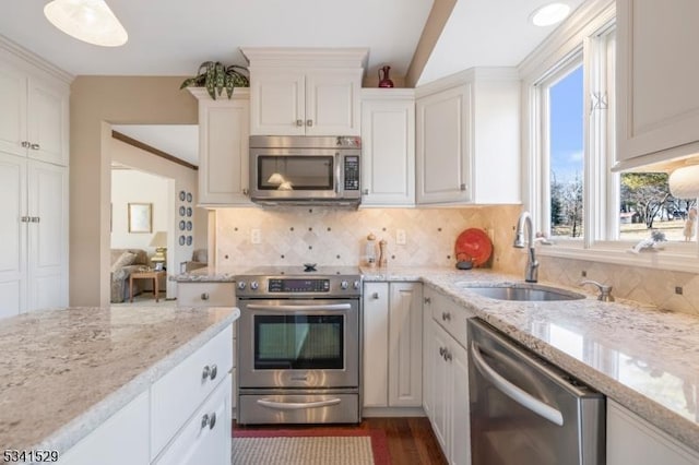 kitchen with stainless steel appliances, a sink, white cabinetry, decorative backsplash, and light stone countertops