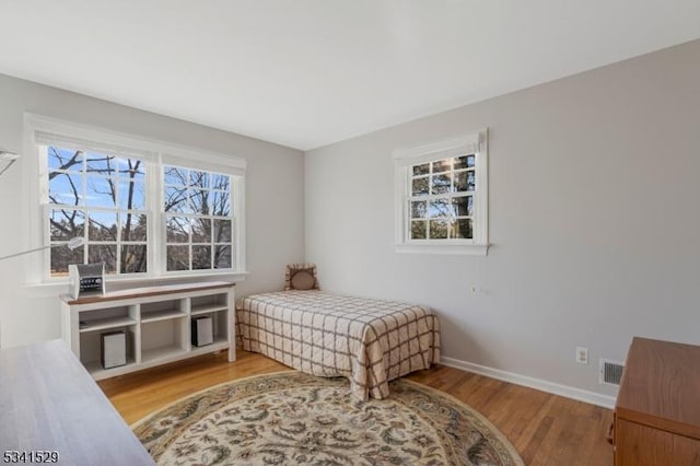 bedroom with baseboards, multiple windows, visible vents, and wood finished floors