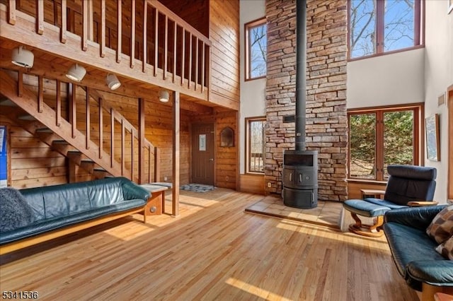 living area featuring stairway, a towering ceiling, a wood stove, wood walls, and wood finished floors