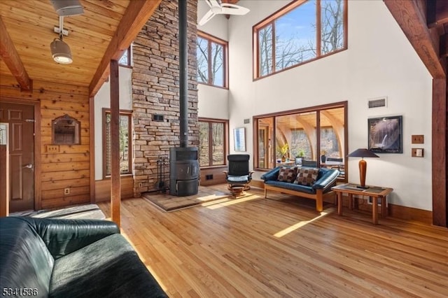 living room featuring lofted ceiling with beams, wooden walls, wood finished floors, wood ceiling, and a wood stove