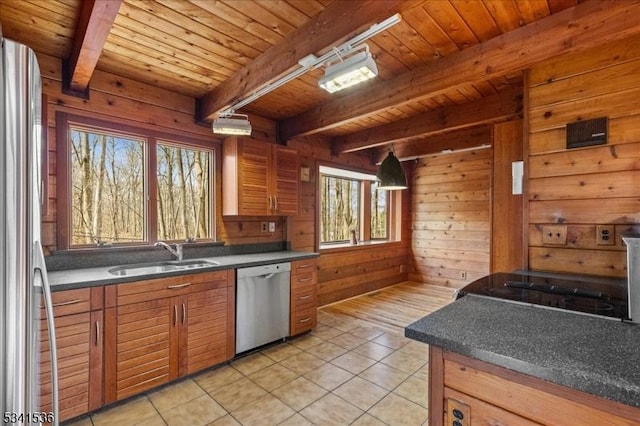 kitchen with wooden walls, a sink, appliances with stainless steel finishes, brown cabinets, and dark countertops