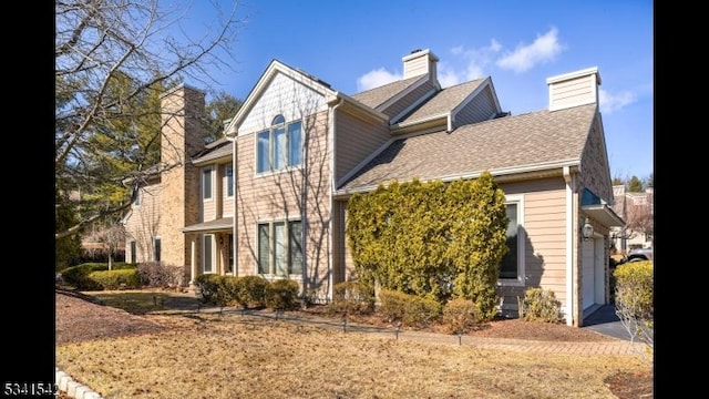 view of side of home featuring an attached garage, a chimney, aphalt driveway, and roof with shingles