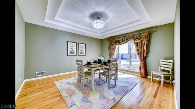 dining area with wood finished floors, visible vents, baseboards, a tray ceiling, and an inviting chandelier