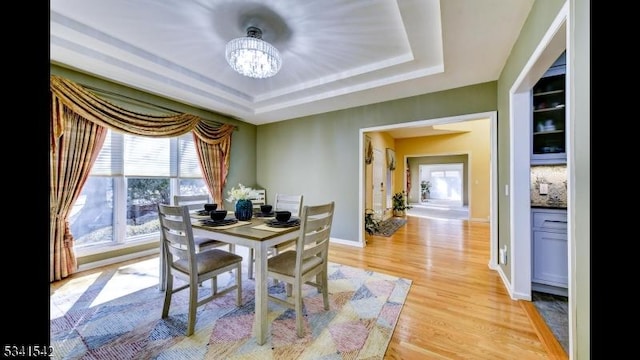 dining space with an inviting chandelier, light wood-style flooring, a tray ceiling, and baseboards