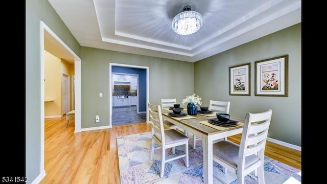 dining area with a chandelier, a tray ceiling, light wood-style flooring, and baseboards