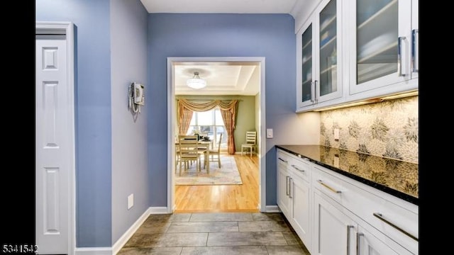 kitchen with wood finished floors, white cabinetry, tasteful backsplash, dark stone countertops, and glass insert cabinets