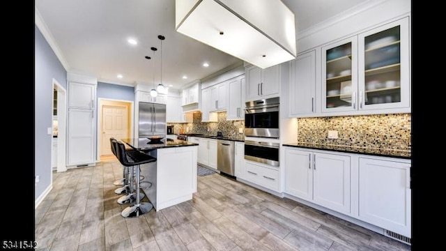 kitchen featuring appliances with stainless steel finishes, glass insert cabinets, ornamental molding, light wood-type flooring, and backsplash