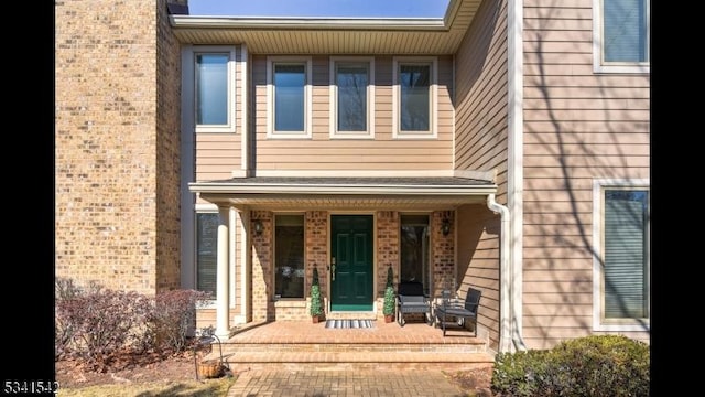 view of exterior entry featuring covered porch and brick siding