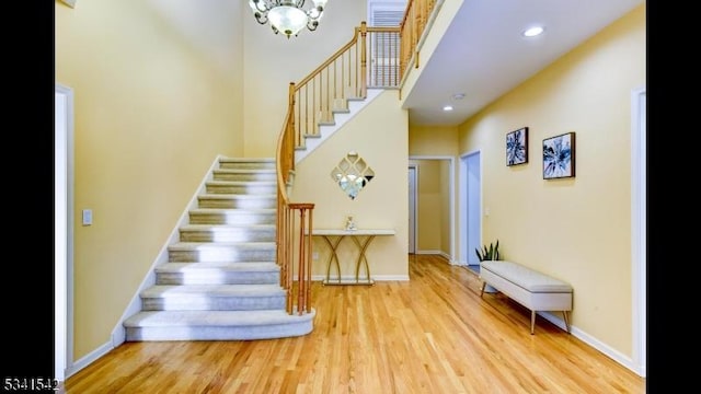 stairs featuring baseboards, a towering ceiling, wood finished floors, a notable chandelier, and recessed lighting