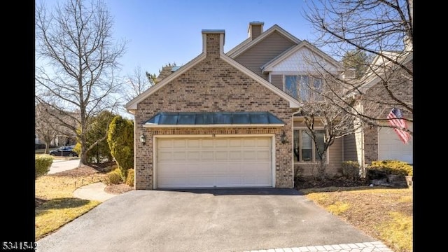 view of front of home with aphalt driveway, an attached garage, brick siding, a standing seam roof, and a chimney