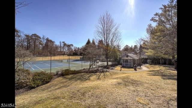 view of tennis court with a lawn and fence