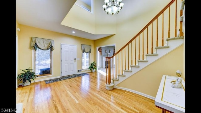 entrance foyer with baseboards, wood finished floors, a high ceiling, stairs, and a notable chandelier