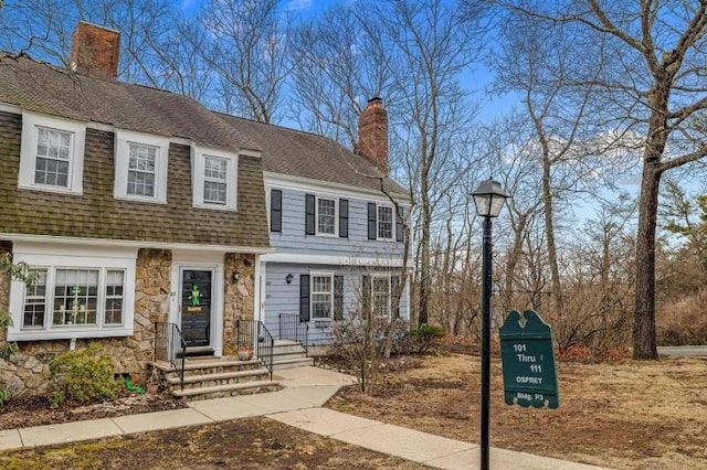 view of front of home featuring stone siding, a chimney, and roof with shingles