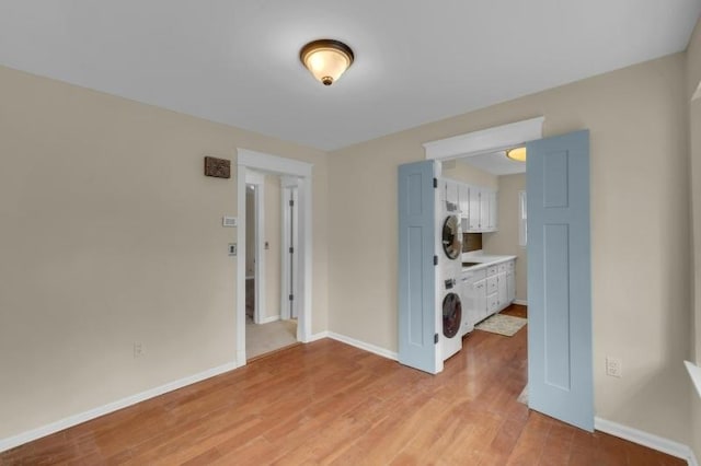 empty room with light wood-type flooring, stacked washer / drying machine, and baseboards