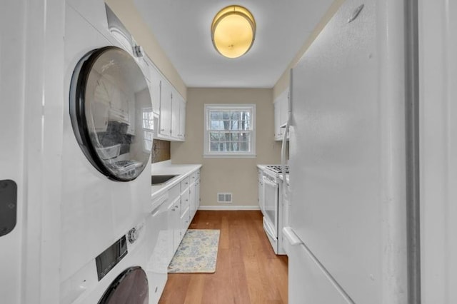 kitchen with visible vents, stacked washer and dryer, white appliances, white cabinets, and light countertops