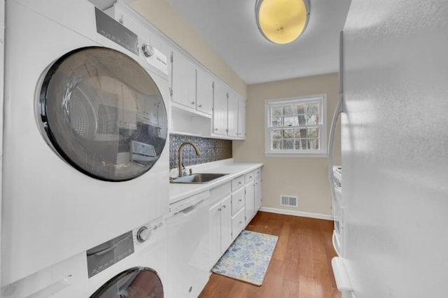 laundry area with visible vents, stacked washer and clothes dryer, a sink, wood finished floors, and baseboards