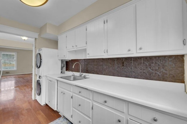 kitchen featuring stacked washer and clothes dryer, a sink, tasteful backsplash, wood finished floors, and light countertops