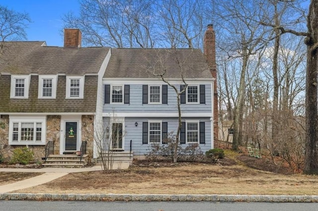 view of property featuring stone siding, roof with shingles, and a chimney