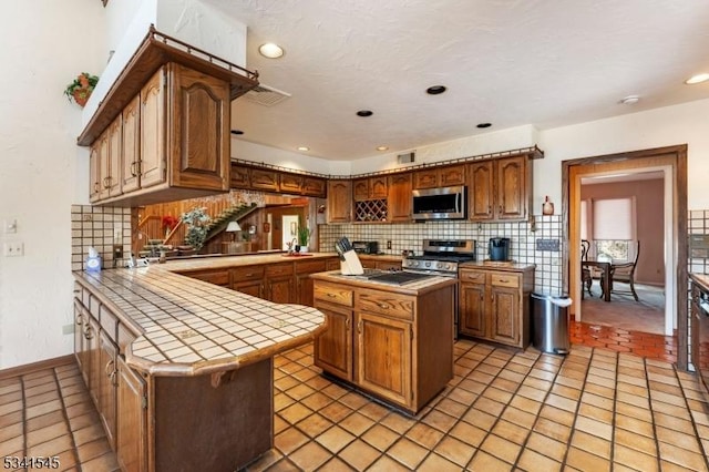 kitchen with tile countertops, a peninsula, visible vents, appliances with stainless steel finishes, and backsplash