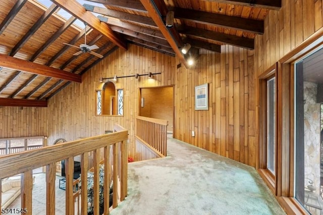 hall featuring lofted ceiling with skylight, wooden ceiling, an upstairs landing, carpet floors, and wood walls