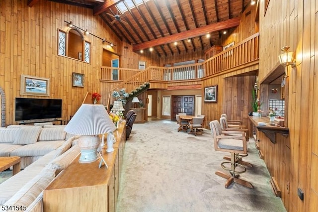 living room with high vaulted ceiling, wooden walls, stairs, beam ceiling, and carpet