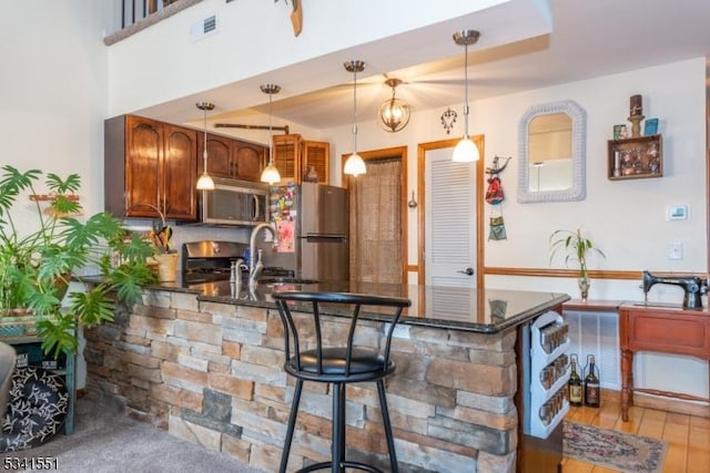 kitchen featuring visible vents, appliances with stainless steel finishes, a peninsula, hanging light fixtures, and a sink