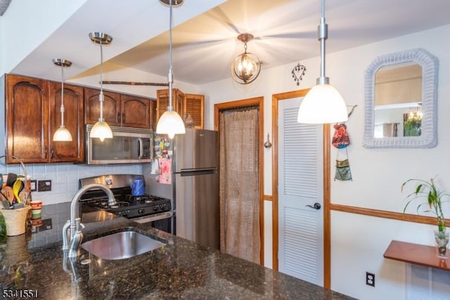 kitchen featuring a sink, appliances with stainless steel finishes, tasteful backsplash, dark stone countertops, and pendant lighting