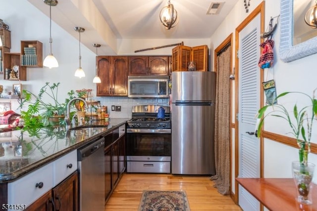 kitchen featuring stainless steel appliances, a sink, visible vents, decorative backsplash, and light wood finished floors