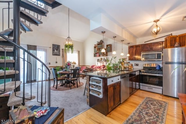 kitchen featuring a peninsula, a sink, appliances with stainless steel finishes, light wood-type flooring, and dark countertops