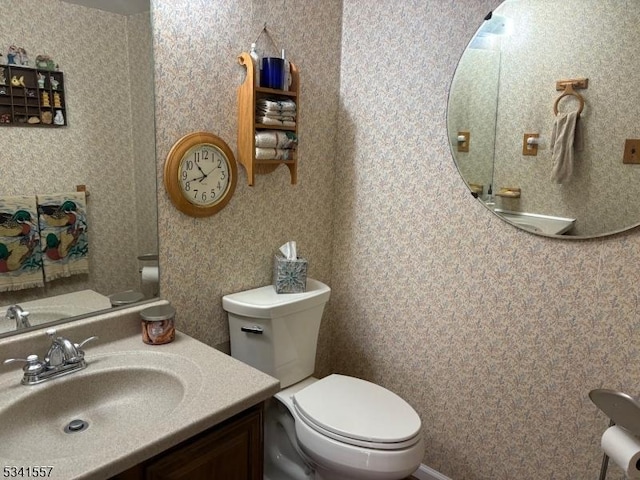 half bath with vanity, toilet, and wallpapered walls