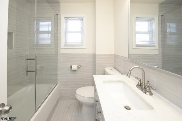 full bathroom featuring tile walls, combined bath / shower with glass door, vanity, and toilet