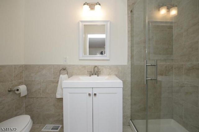 bathroom with a stall shower, vanity, visible vents, and tile walls