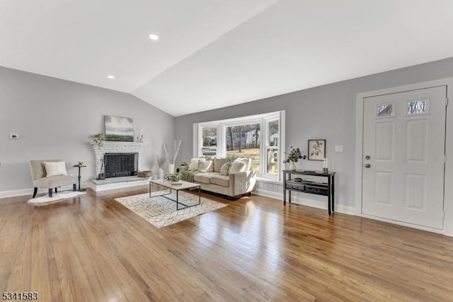 living room featuring lofted ceiling, a brick fireplace, wood finished floors, and baseboards