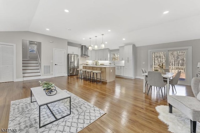 living area featuring lofted ceiling, visible vents, light wood-style flooring, and a healthy amount of sunlight