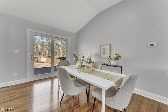 dining space with vaulted ceiling, wood finished floors, visible vents, and baseboards