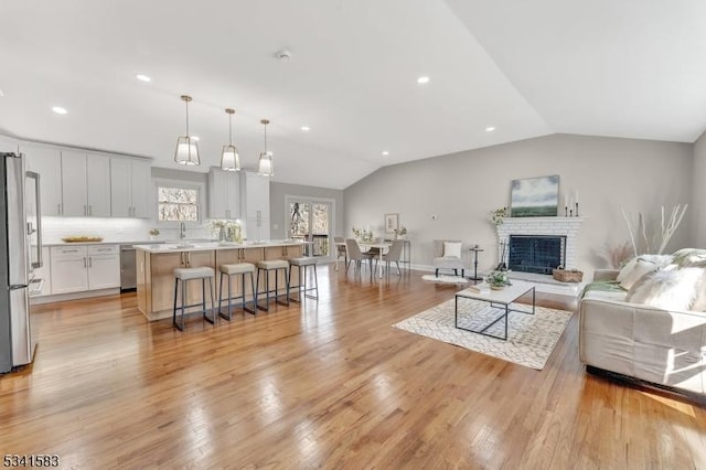 living room with vaulted ceiling, recessed lighting, a brick fireplace, and light wood-style floors