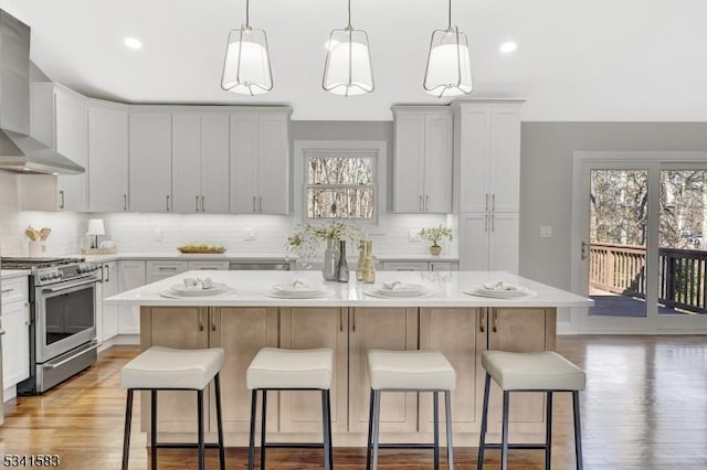 kitchen with a kitchen bar, high end stove, a kitchen island, and wall chimney exhaust hood