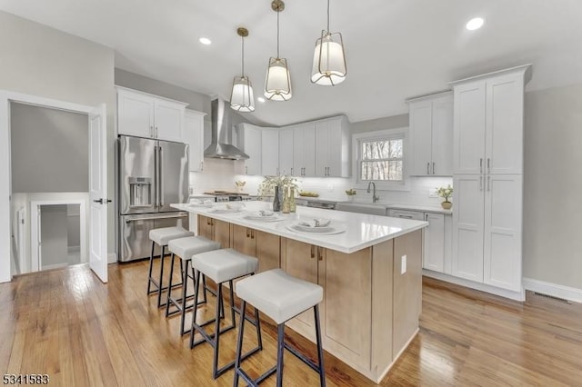 kitchen with a kitchen island, a kitchen breakfast bar, high end fridge, wall chimney range hood, and light countertops