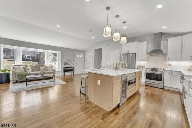 kitchen with beverage cooler, wall chimney exhaust hood, vaulted ceiling, and stainless steel appliances