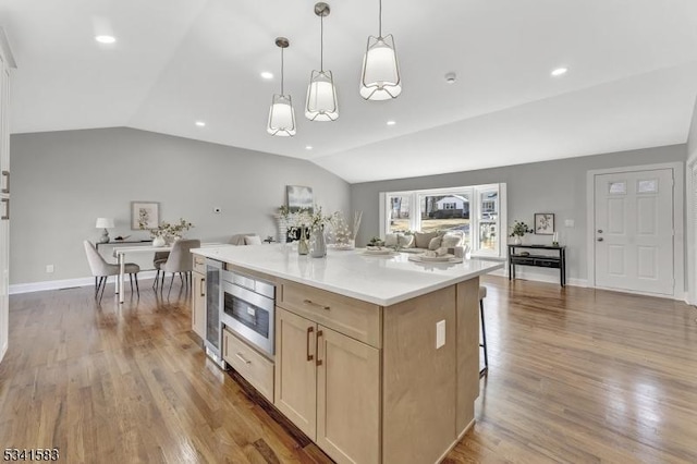 kitchen featuring lofted ceiling, stainless steel microwave, light brown cabinets, and wood finished floors