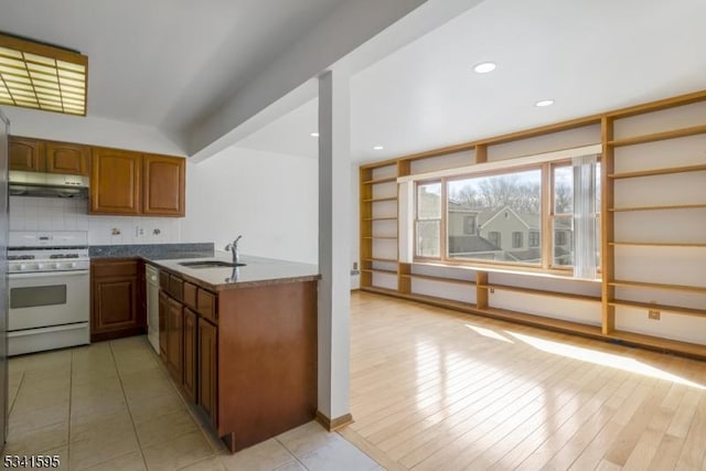 kitchen with brown cabinetry, white range with gas cooktop, a sink, decorative backsplash, and under cabinet range hood