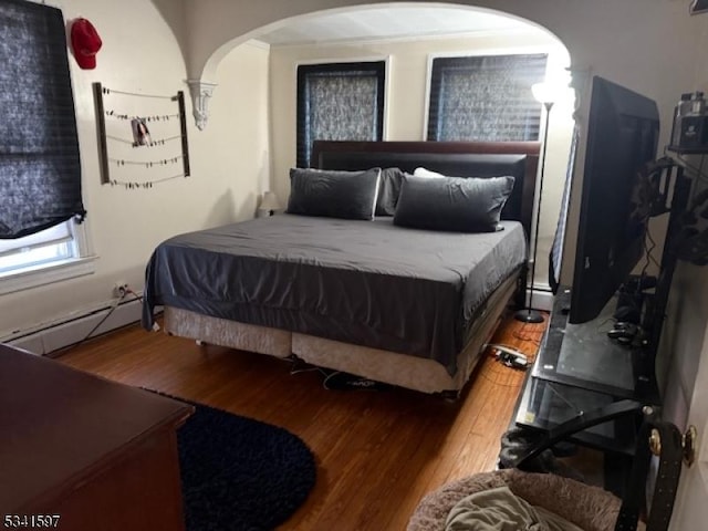 bedroom featuring arched walkways, a baseboard radiator, and wood finished floors