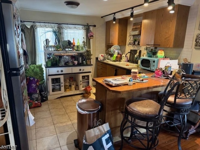 kitchen with light tile patterned floors, a sink, brown cabinets, freestanding refrigerator, and decorative backsplash