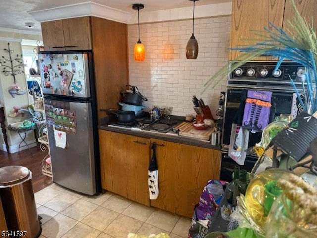 kitchen with cooktop, decorative backsplash, dark countertops, brown cabinets, and freestanding refrigerator