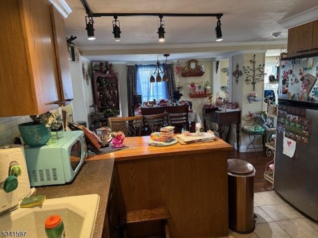 kitchen featuring white microwave, light tile patterned flooring, a peninsula, freestanding refrigerator, and crown molding