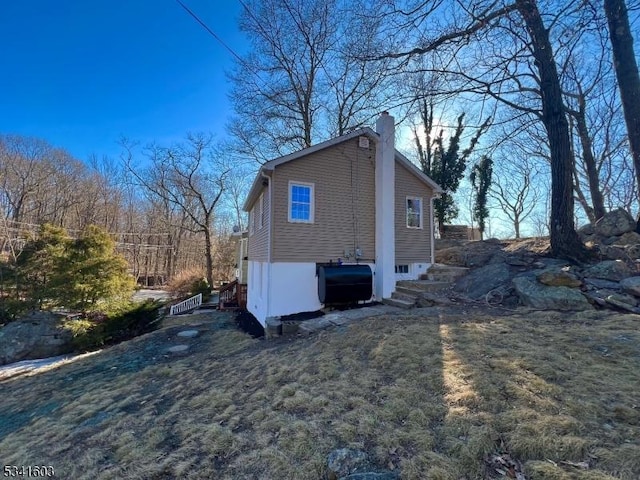 view of side of property with heating fuel, a chimney, and a lawn