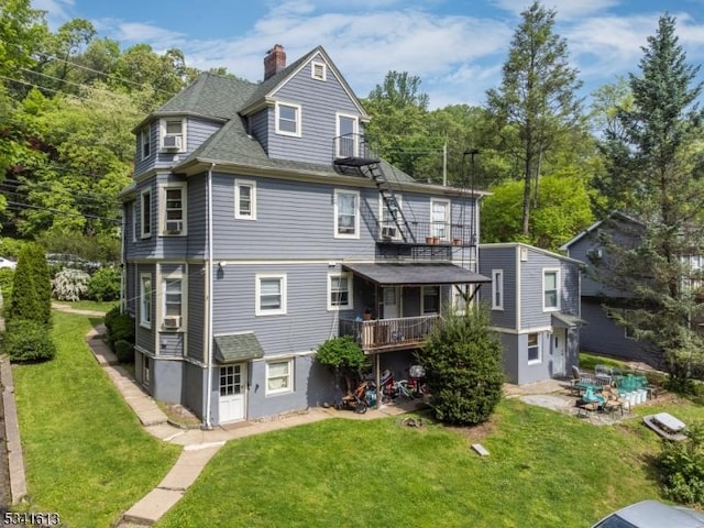 back of property featuring roof with shingles, a chimney, a lawn, and a patio